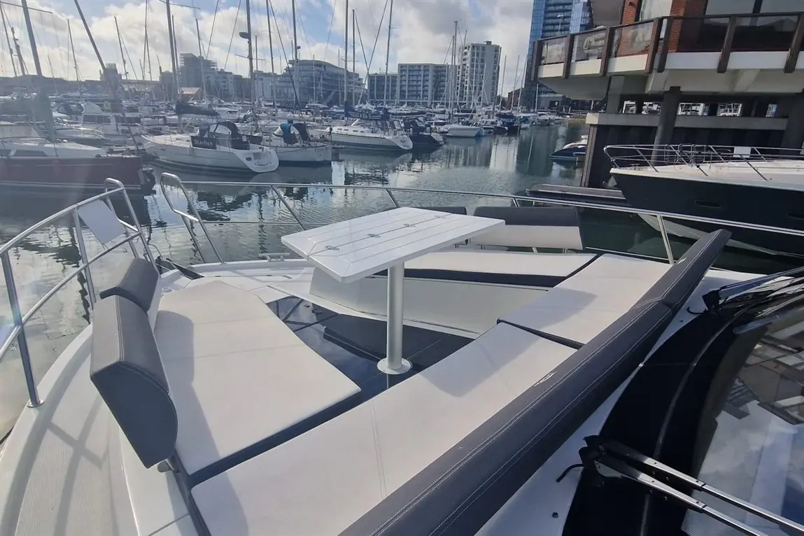 Comfortable seating on a yacht with a table, overlooking a marina filled with boats and modern buildings in the background.